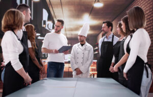 A restaurant manager with a clipboard addressing a group of diverse kitchen and service employees, demonstrating what is temporary staffing in the hospitality industry.
