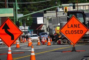 Certified flaggers managing traffic control with lane closed signage, cones, and construction equipment to ensure road safety during active work zone operations.