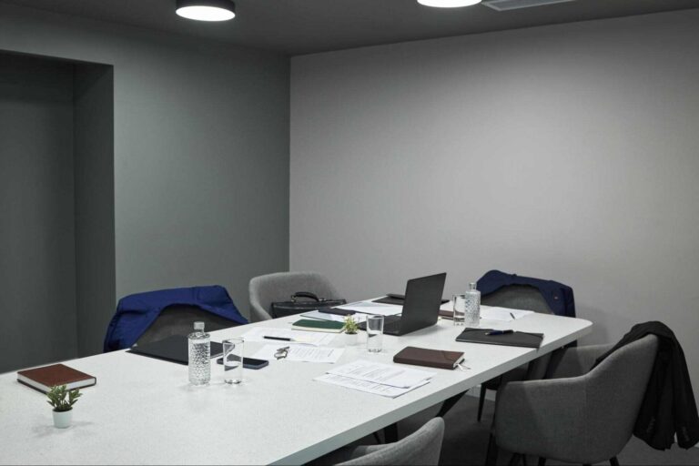 Modern office meeting room with several empty chairs around a conference table, illustrating the cost of being understaffed through unfilled workspaces and reduced team capacity.