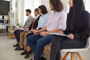 Job candidates seated in a waiting area holding resumes and application documents, illustrating the hiring candidates process, candidate screening, recruitment interviews, and talent acquisition strategies.