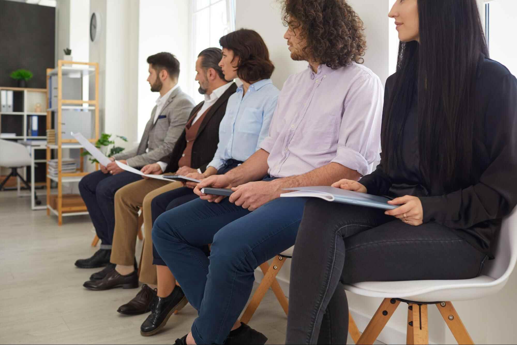 Job candidates seated in a waiting area holding resumes and application documents, illustrating the hiring candidates process, candidate screening, recruitment interviews, and talent acquisition strategies.
