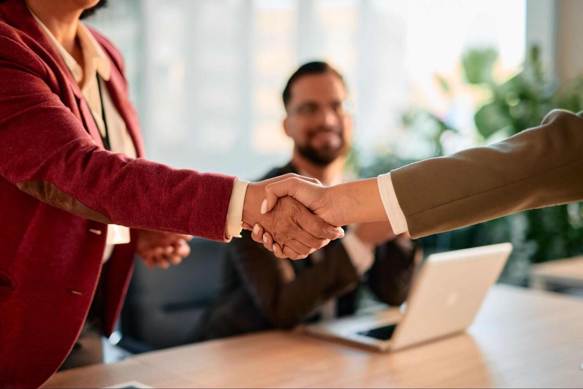 Hiring manager and successful candidate shaking hands across a conference table, representing temporary vs direct hire recruitment and strategic staffing decisions for business growth.